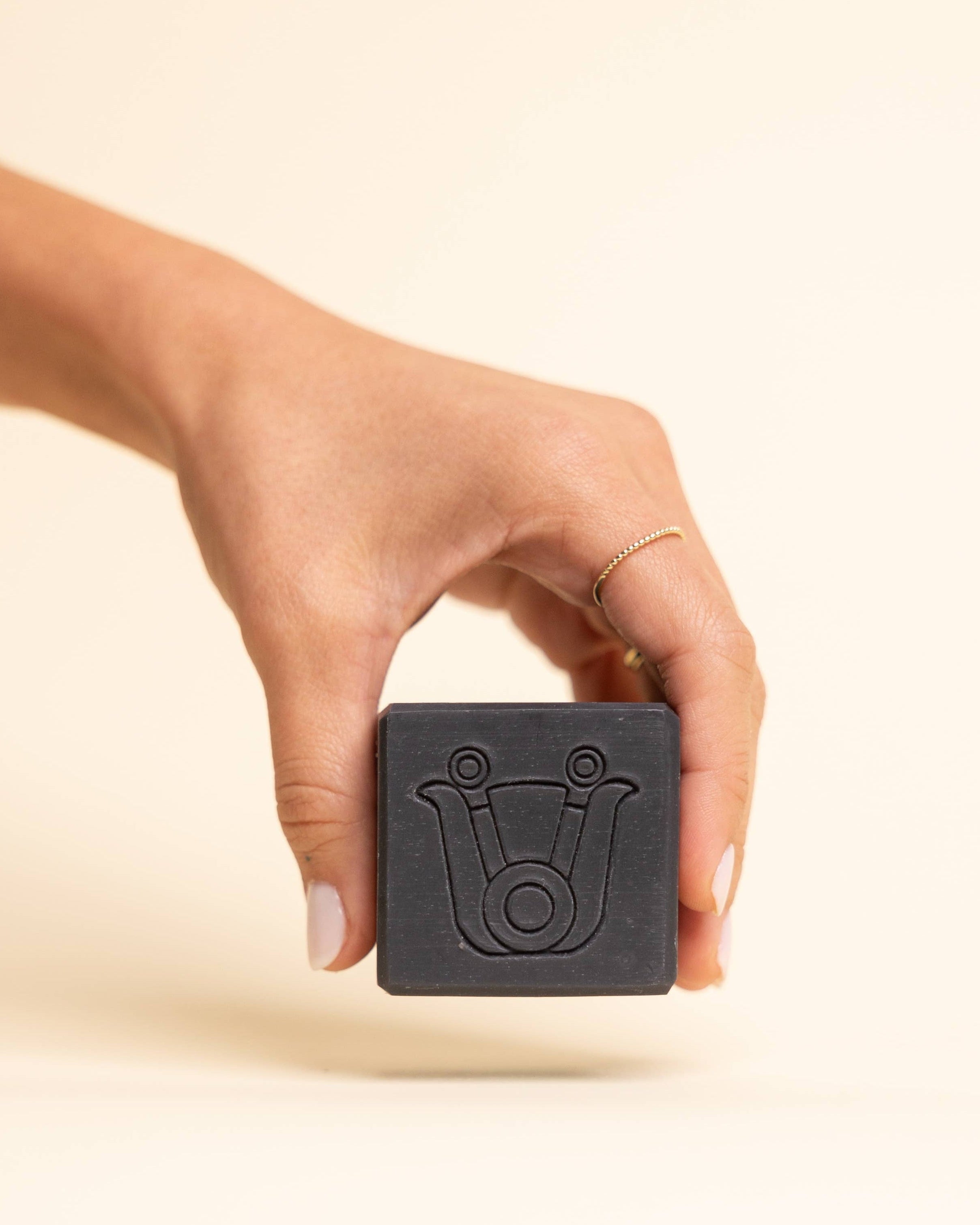 Hand holding a black square soap bar with a logo on a beige background